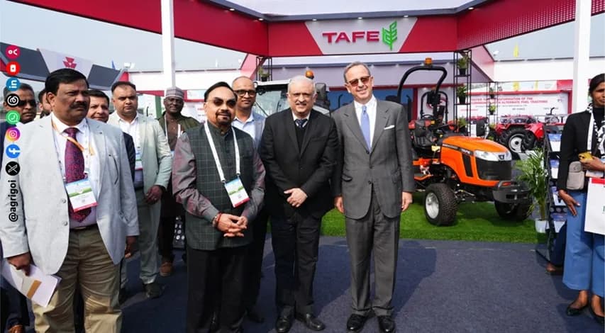 Delegates beside a tractor on an exhibitor stand at an agricultural machinery fair.