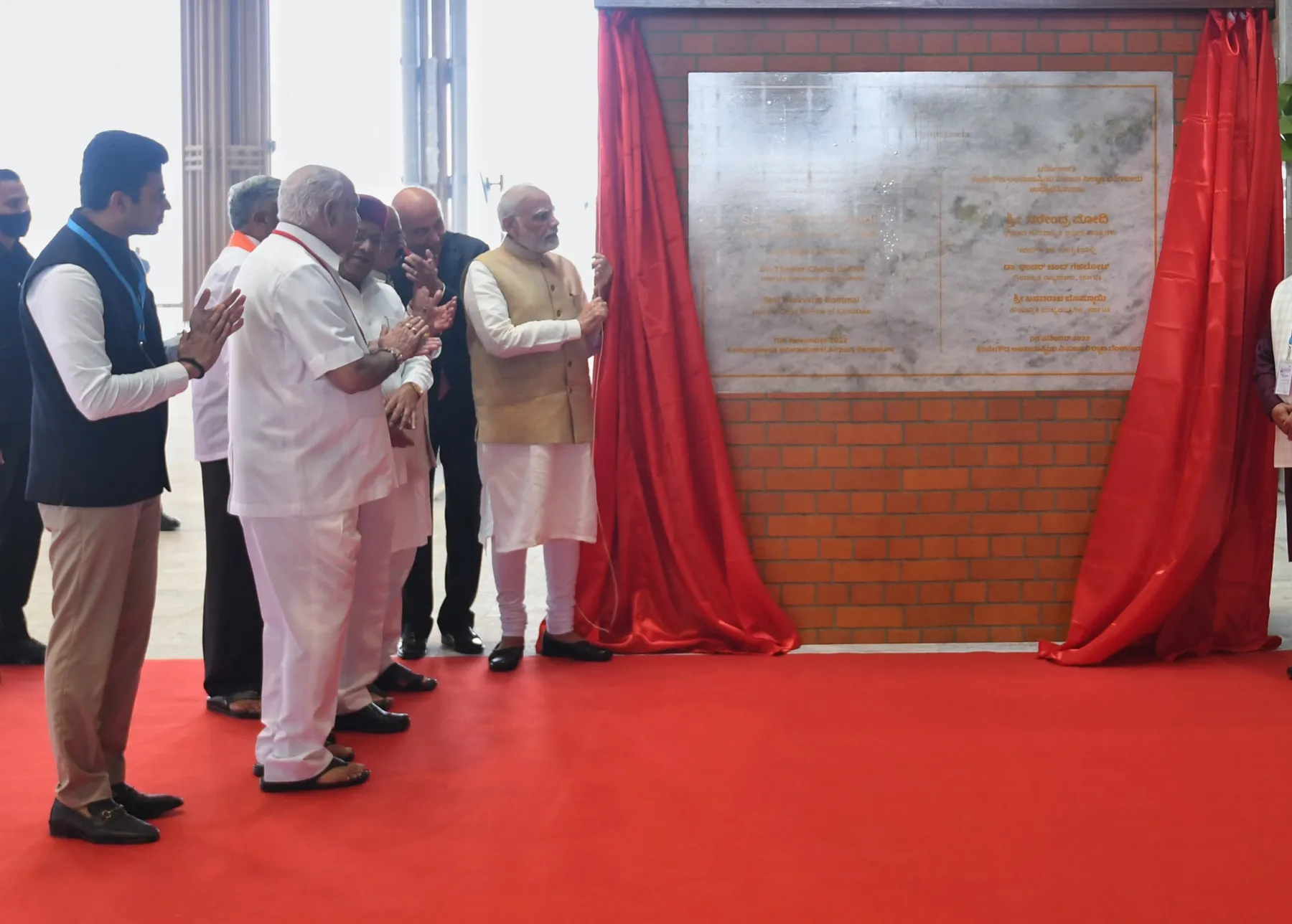 A ceremonial plaque unveiling on a red-carpeted dais, the drape drawn back before assembled dignitaries.