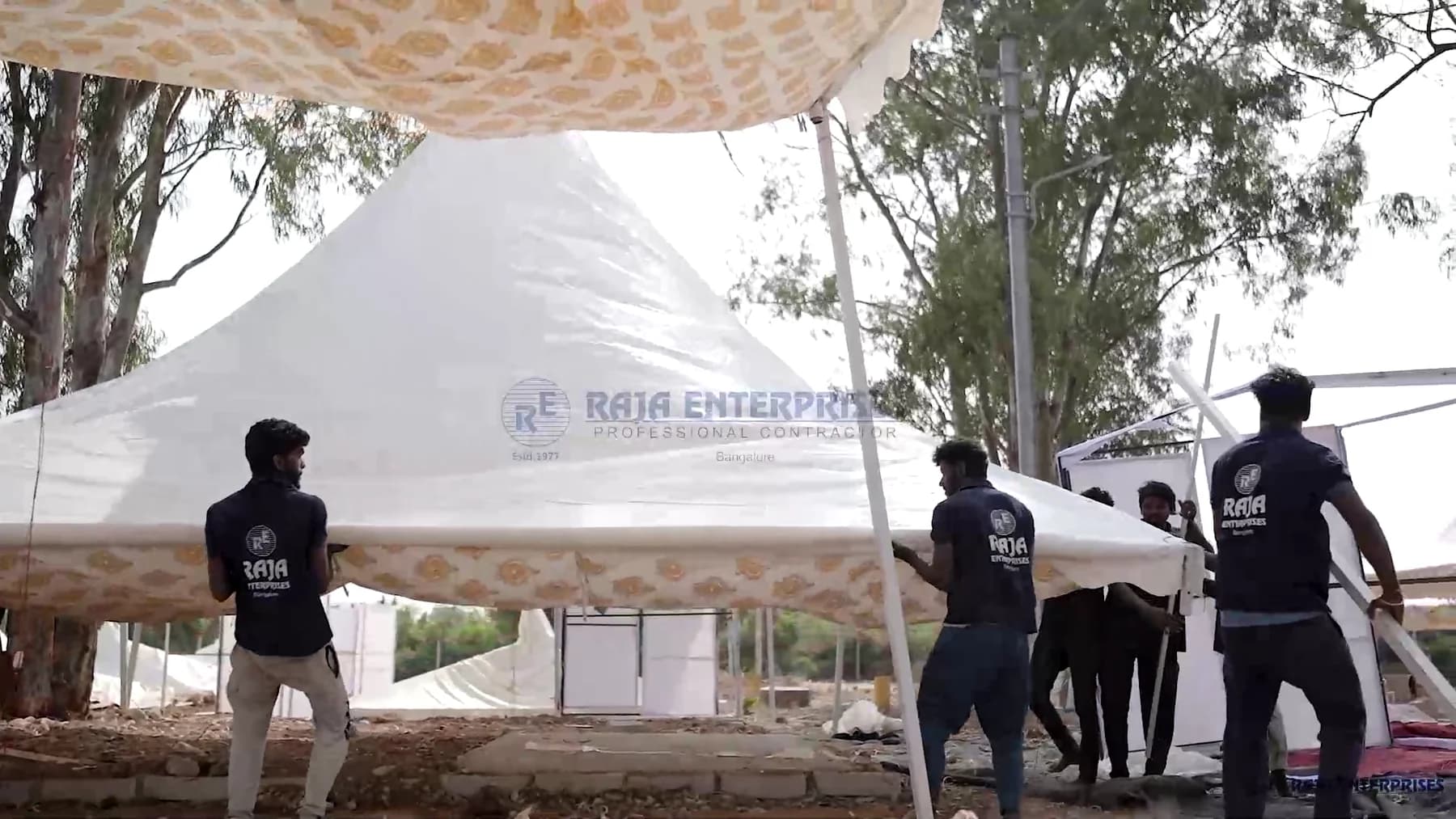 Raja Enterprises crew in branded shirts raising a canopy structure on site during a build.