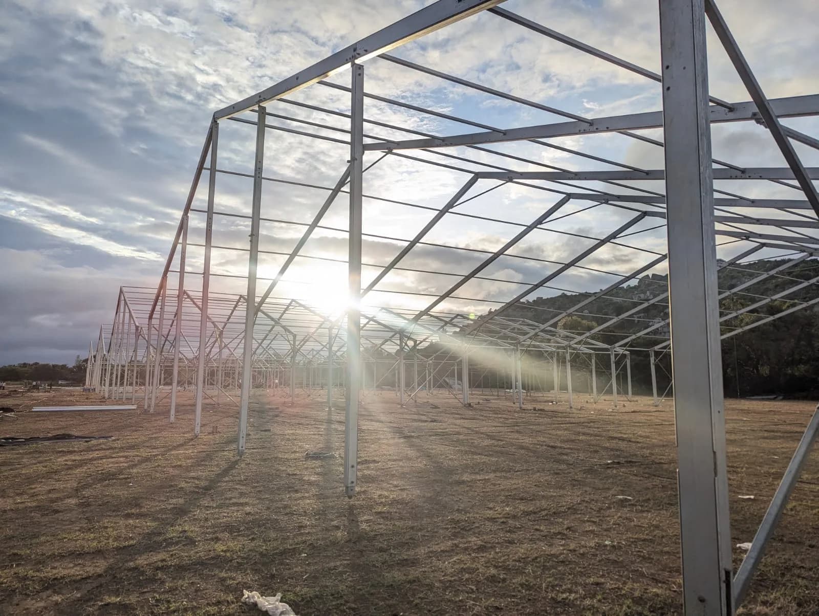 A German hanger frame part-erected on open ground at sunrise, its aluminium portal frames standing unclad against the sky.