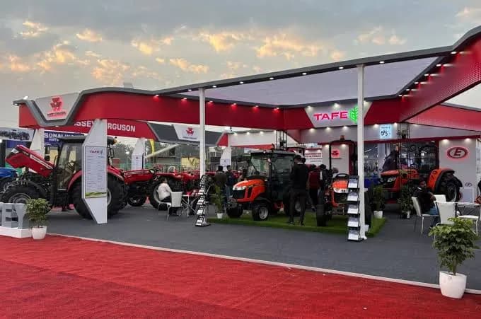 An outdoor exhibition ground at dusk, machinery displays under exhibitor structures.