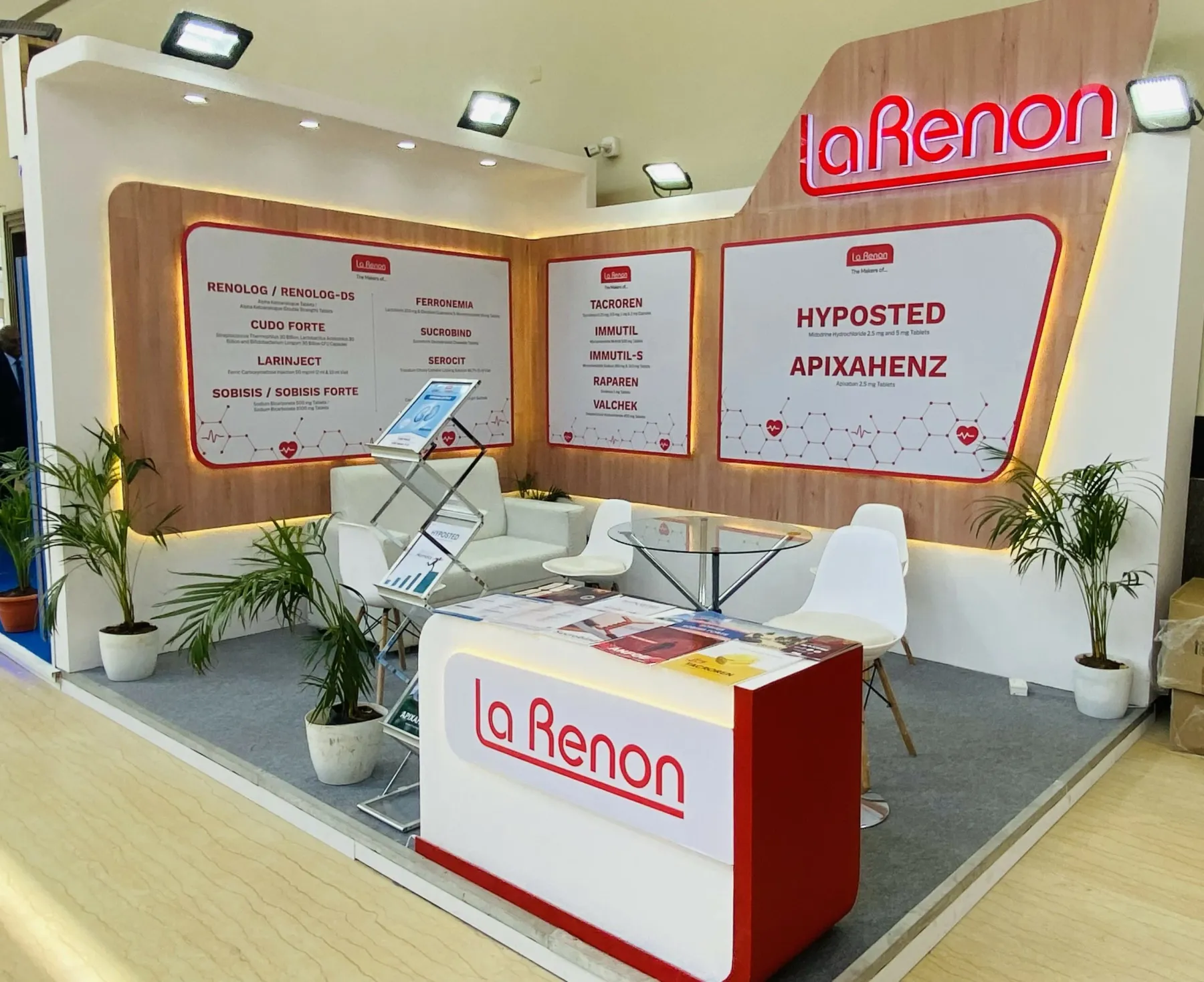 An exhibition stall interior: branded back wall, display counters, seating and planting.