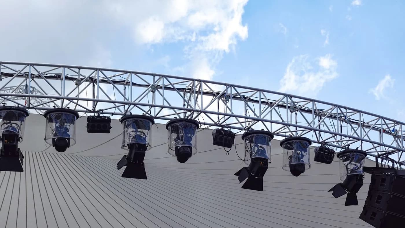 Truss-mounted lighting and line-array speakers rigged above an open-air stage.